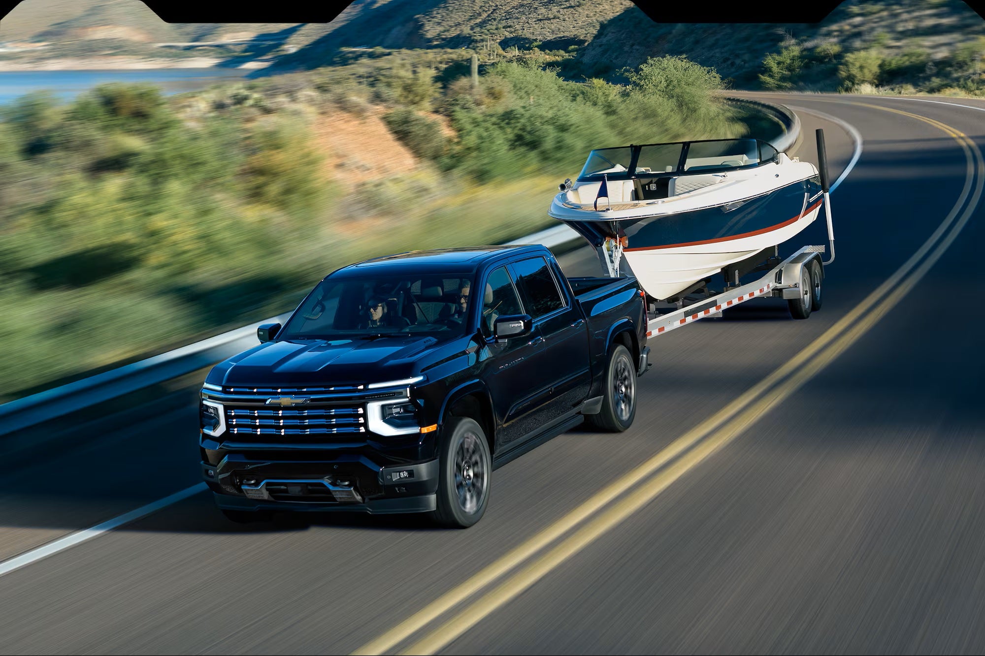 2027 Chevrolet Silverado High Country towing a boat on a mountain highway